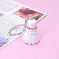 Detailed close-up of a white shuttlecock keychain with red trim on pink background - White
