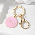 Detailed macro view of golden Honey letter heart keychain with pink enamel finish - Pink Round Honey