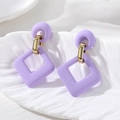Gros plan de boucles d'oreilles carrées violettes mates sur un plateau blanc texturé - Boucles d'Oreilles Carrées / Violet