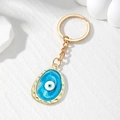 Macro detail van gouden evil eye hanger met kleurrijk emaille hars druppeleffect - Blauw Ovaal Oog
