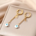 Detailed view of gold evil eye drop earrings with cross chain on a jewelry stand - White Eye Flower Charm / Gold