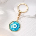 Goldener Schlüsselanhänger mit blau-weißem Evil Eye Harzanhänger auf weißem Sockel präsentiert - Blau Rund