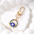 Detailansicht goldener Evil Eye Schlüsselanhänger mit bunten Strasssteinen auf Steinplatte - Königsblaues Evil Eye