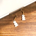 Detail eines weißen Bären-Ohrrings mit goldenem Metallhaken auf Holzgrund - Weißer Bär