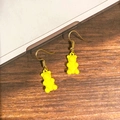 Detail von gelben Gummibärchen-Ohrringen mit Goldhaken auf dunklem Holzhintergrund - Gelber Bär