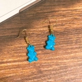 Detailansicht hellblauer Gummibärchen-Ohrhänger mit goldenen Haken auf Holzgrund - Blauer Bär
