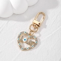 Golden heart keychain with crystal LOVE letter and blue evil eye charms on white surface - White