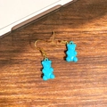 Detailed close-up of blue gummy bear earrings with golden metal hooks on a wood surface - Sky Blue Bear