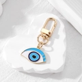 Goldener Schlüsselanhänger mit blauem Auge-Herz-Anhänger auf weißem Displayständer - Blau und Weiß Auge Gold
