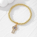 Beaded gold bracelet with evil eye cross pendant on a textured white stone surface - Royal Blue Eye Cross