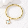 Golden beaded bracelet with a sparkling clover evil eye charm on a white stone background - Four-leaf Clover / White Eye Flower