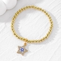 Detailed macro view of a gold beaded bracelet with a sparkling crystal evil eye star charm - Five-pointed Star / Royal Blue Eye Star