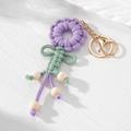 Detail eines handgewebten lila Blumen-Schlüsselanhängers mit Holzperlen und Goldkarabiner - Lila Blume