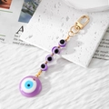 Detail view of purple Evil Eye beaded keychain with golden lobster clasp on marble stone - Purple