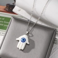 Hamsa Hand necklace with blue Evil Eye pendant on a silver chain displayed on jewelry box - White