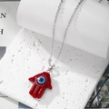 Red Hamsa Hand necklace with blue evil eye pendant on white stone podium background - Burgundy