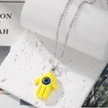 Detail of yellow Hamsa Hand pendant with a blue evil eye on a silver chain necklace - Yellow