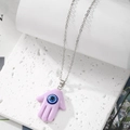 Detailed macro view of a lavender Hamsa hand pendant with a blue evil eye on silver chain - Light Purple