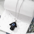 Macro shot of Hamsa hand pendant with blue evil eye on white marble background - Black