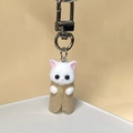 Close-up of a cute white flocked kitten keychain with a khaki shawl and silver metal clasp - Camel