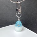 Macro view of a cute blue chick hatching from an eggshell with a silver lobster clasp - Blue