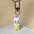 Detailed macro view of a white flocked kitten keychain in a yellow felt wrap with silver clasp - Light Yellow