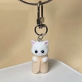 Close-up of a cute handmade white flocked cat plush keychain in a beige felt burrito wrap - Nude