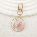 Détail d'une marguerite rose séchée dans un pendentif en résine avec bordure dorée - Marguerite rose demi