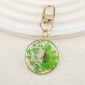Vue détaillée d'un porte-clés doré en résine avec fleurs séchées vertes et perle - Marguerite verte demi
