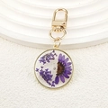 Détail de pendentif doré rond avec de vraies fleurs séchées violettes en résine - Marguerite violette demi