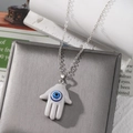 Silver chain necklace with a white Hamsa hand pendant and blue evil eye resin charm - Gray