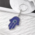 Hand van Fatima sleutelhanger met blauwe steentjes en boze oog op een wit plateau - Koningsblauw Zilveren Hand