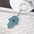 Hamsa Hand sleutelhanger met blauwe strassteentjes op een witte gegolfde achtergrond - Meerblauw Zilveren Hand