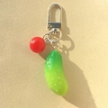 Gros plan sur le porte-clés cornichon en résine avec fermoir argenté et breloque rouge - Concombre et Tomate
