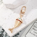 Porte-clés arête de poisson doré avec amulette œil bleu sur un présentoir en pierre chic - Oeil Blanc Arête de Poisson