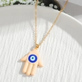 Golden Hamsa Hand necklace with blue Evil Eye pendant on a decorative white tray - Nude Hand