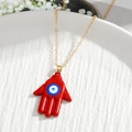 Golden Hamsa hand necklace with red evil eye pendant displayed on a white tray - Red Hamsa Hand