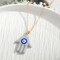 Golden Hamsa hand necklace with grey enamel and blue evil eye charm on a white plate - Grey Hamsa Hand