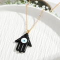 Close-up of black Hamsa Hand pendant with Evil Eye on a gold chain over ceramic - Black Hamsa Hand