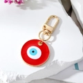 Round red enamel evil eye keychain with gold clasp on white stone background - Red Evil Eye