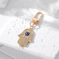Hamsa-Hand und Evil-Eye-Schlüsselanhänger mit Kristallen auf weißem Stein - Hand der Fatima Stil / Gold Blau Rosa Auge