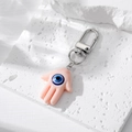Porte-clés main de Fatma en résine rose avec œil bleu sur une texture de pierre blanche - Rose Clair
