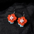 Gros plan de boucles d'oreilles fleurs en acrylique aux pétales orange sur tulle noir - Fleur Rouge (Crochet en Argent)