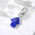 Blauer Hamsa Hand Schlüsselanhänger mit Evil Eye und Silberclip auf weißem Naturstein - Königsblau