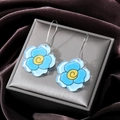Detailansicht der blauen Acryl-Blumenohrringe mit gelber Mitte auf grauer Satinbox - Blaue Blume