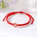 Detailed shot of handmade woven red rope bracelet with evil eye pendant on stone base - Red
