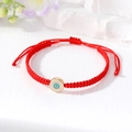 Macro shot of handmade red woven Evil Eye bracelet with polished gold-tone metal pendant - White