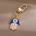 Hamsa-Hand-Schlüsselanhänger mit blauem Auge-Anhänger und Strasssteinen auf braunem Seidenstoff - Stachelige Hand der Fatima / Gold