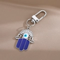 Hamsa Hand Schlüsselanhänger mit blauem Auge Detail auf seidigem Stoffhintergrund - Hohle Handfläche / Silber