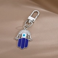 Portachiavi Mano di Fatima Evil Eye con smalto blu su sfondo di raso marrone scuro - Portachiavi Mano di Fatima Traforata Argento